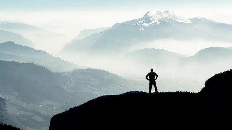 Silhouette d'une personne debout sur une crête avec des montagnes enneigées au loin