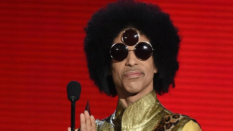 Prince portant une chemise dorée à col et des lunettes de soleil à trois verres