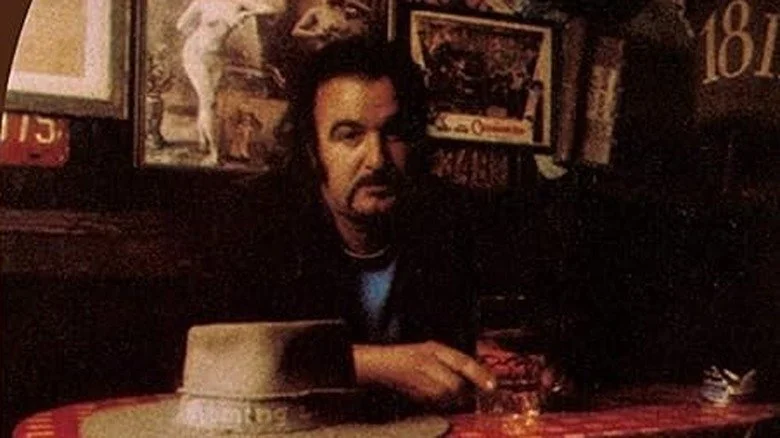 Jim Sullivan avec moustache assis dans un pub avec un verre et un chapeau sur la table