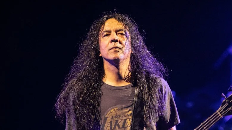 Mike Inez avec une longue chevelure jouant de la guitare sur scène