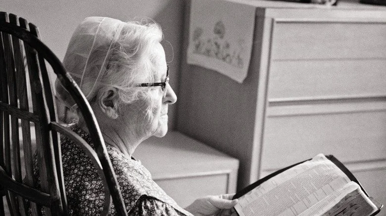 Femme Amish âgée assise lisant la Bible