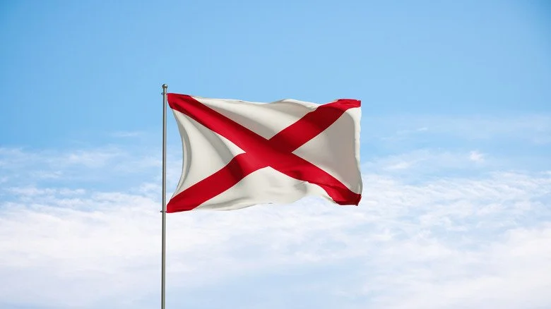 Drapeau de l'Alabama contre un ciel bleu pâle avec des nuages blancs