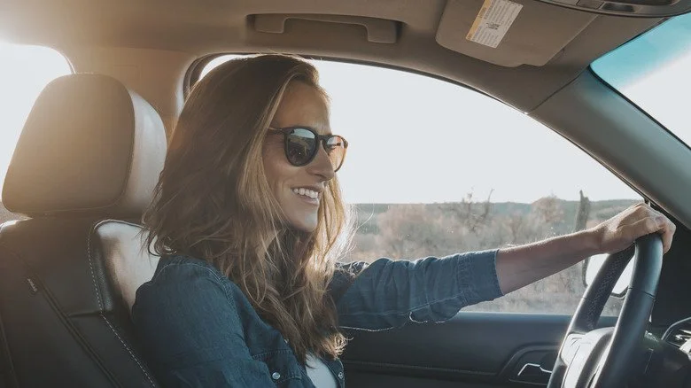 Une femme souriante avec des lunettes de soleil au volant
