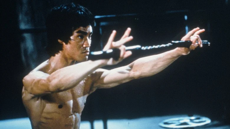 Bruce Lee tenant une arme devant lui dans Enter the Dragon