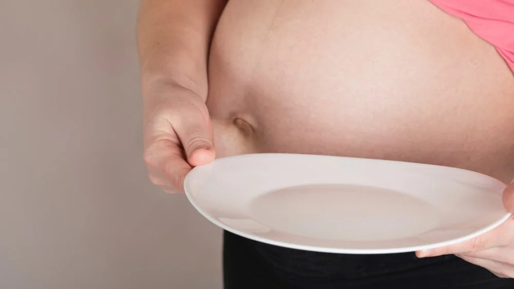 Ventre de femme enceinte avec une assiette vide