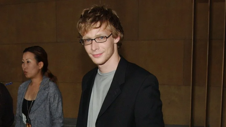 Johnny Lewis souriant en coin face à la caméra