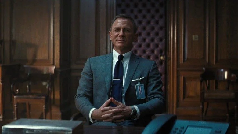Daniel Craig en James Bond avec un sourire en coin assis dans une chaise dans No Time to Die