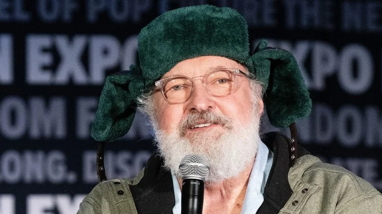 Randy Quaid portant un chapeau en fourrure et tenant un micro