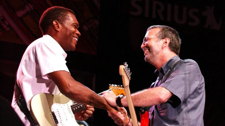 Robert Cray et Eric Clapton se serrant la main avec leurs guitares et souriant