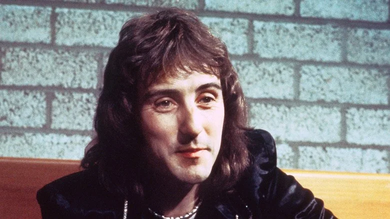 Photo du guitariste Denny Laine devant un mur de briques