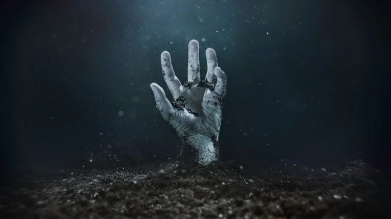 Zombie hand emerging from soil, dark background.