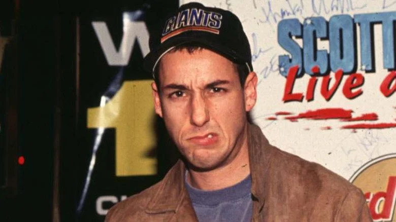 Adam Sandler portant une casquette de baseball et faisant une grimace amusante