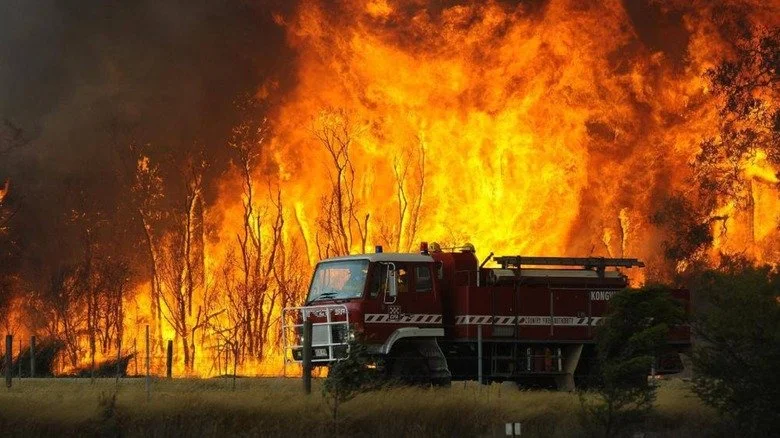 Un camion de pompiers australien devant un feu de brousse en flammes