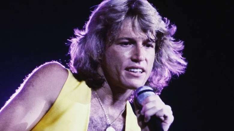 Andy Gibb en veste jaune et médaillon chantant sur scène
