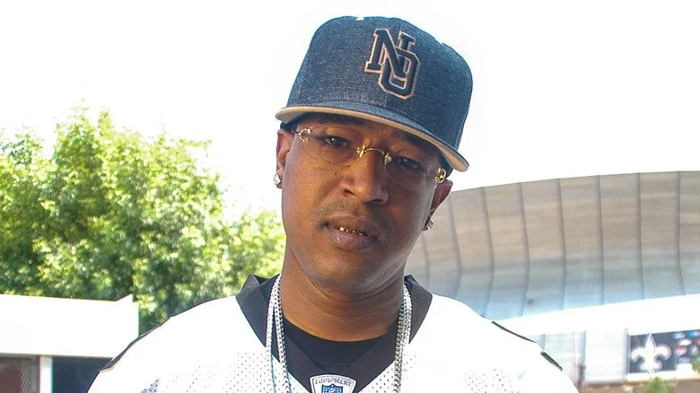 C-Murder portant une casquette bleu et des lunettes, inclinant la tête en extérieur