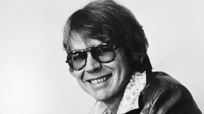 C.W. McCall souriant avec lunettes et veste en cuir