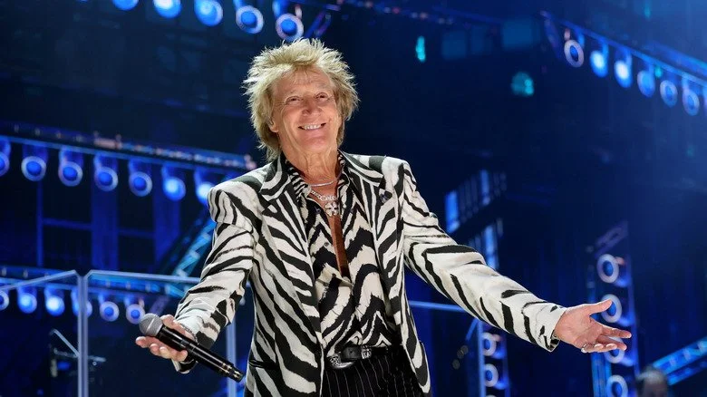Rod Stewart sur scène, bras grands ouverts, en 2025