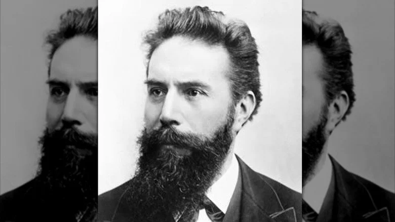 Wilhelm Röntgen avec une longue barbe sombre en costume regardant vers la droite