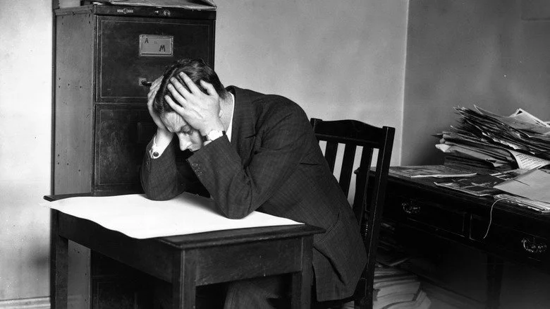 Homme à son bureau, tête entre les mains, image en noir et blanc.