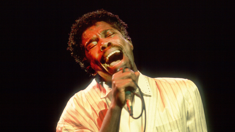 Billy Ocean chantant dans une chemise claire, sur fond sombre