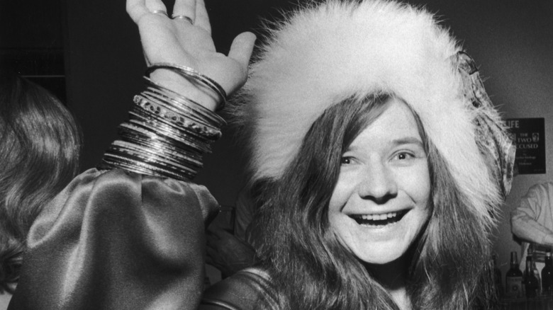 Janis Joplin souriant et saluant avec un chapeau en fourrure