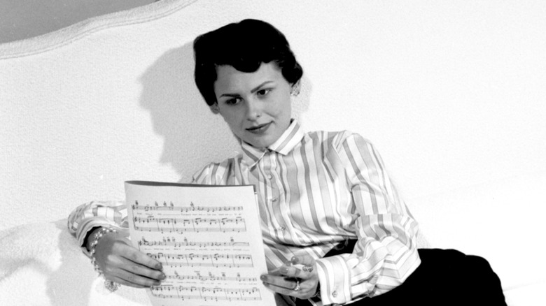 Joan Weber lisant une partition sur un lit blanc