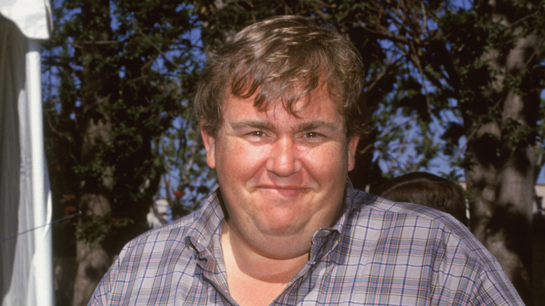 John Candy souriant à l'extérieur en chemise à carreaux