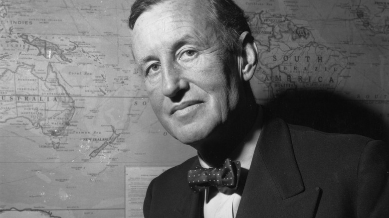 Ian Fleming assis devant une carte au mur
