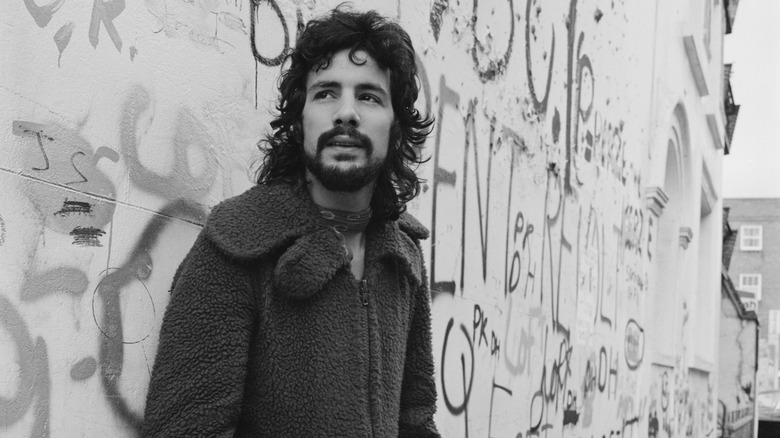 Cat Stevens debout devant un mur couvert de graffitis