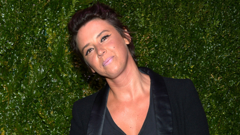 Cat Power souriant en costume noir avec des feuilles en arrière-plan