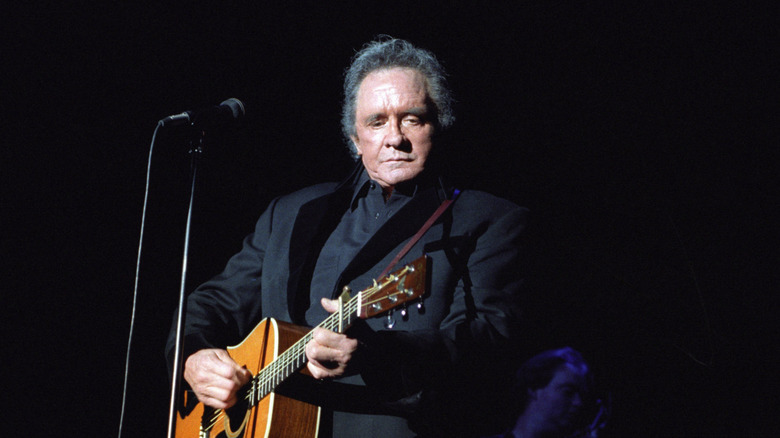 Johnny Cash en costume sombre jouant de la guitare sur scène avec un fond noir