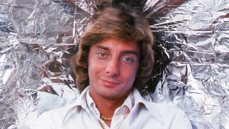 Barry Manilow souriant devant un mur métallisé en 1976