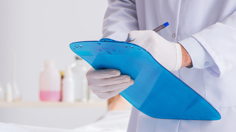 Personnel médical portant des gants et écrivant sur un presse-papiers médical