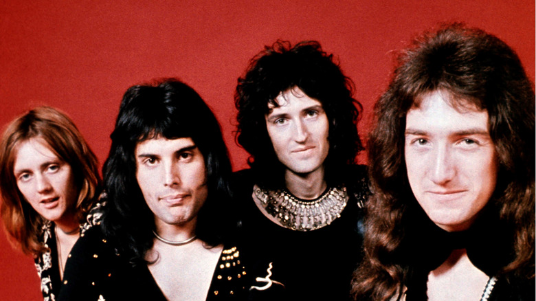 Le groupe Queen posant devant un fond rouge