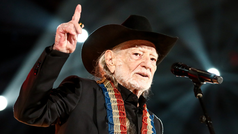 Willie Nelson en costume noir et stetson sur scène, pointant le doigt vers le haut