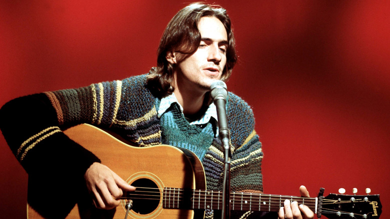 James Taylor chantant et jouant de la guitare les yeux fermés