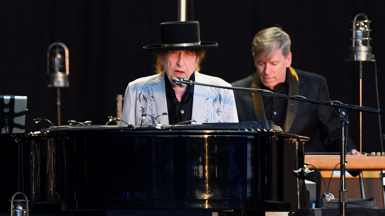 Bob Dylan au piano portant un costume gris et un chapeau noir